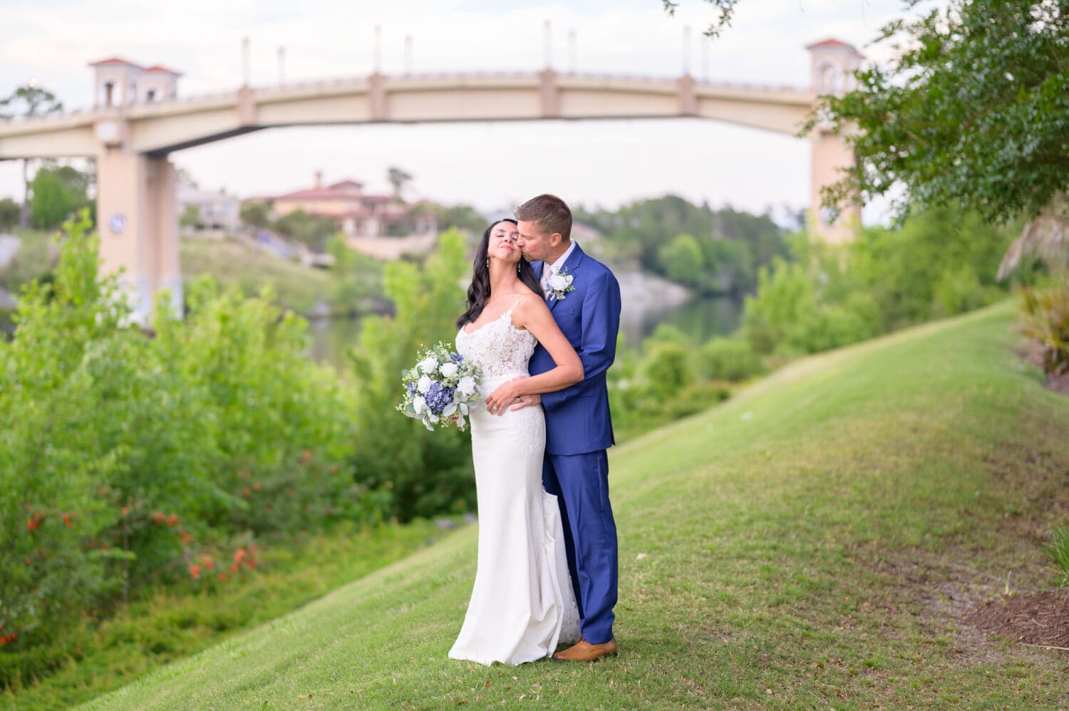 Portraits of bride and groom on the grassy hill with the Grande Dunes bridge in the background - The Marina Inn