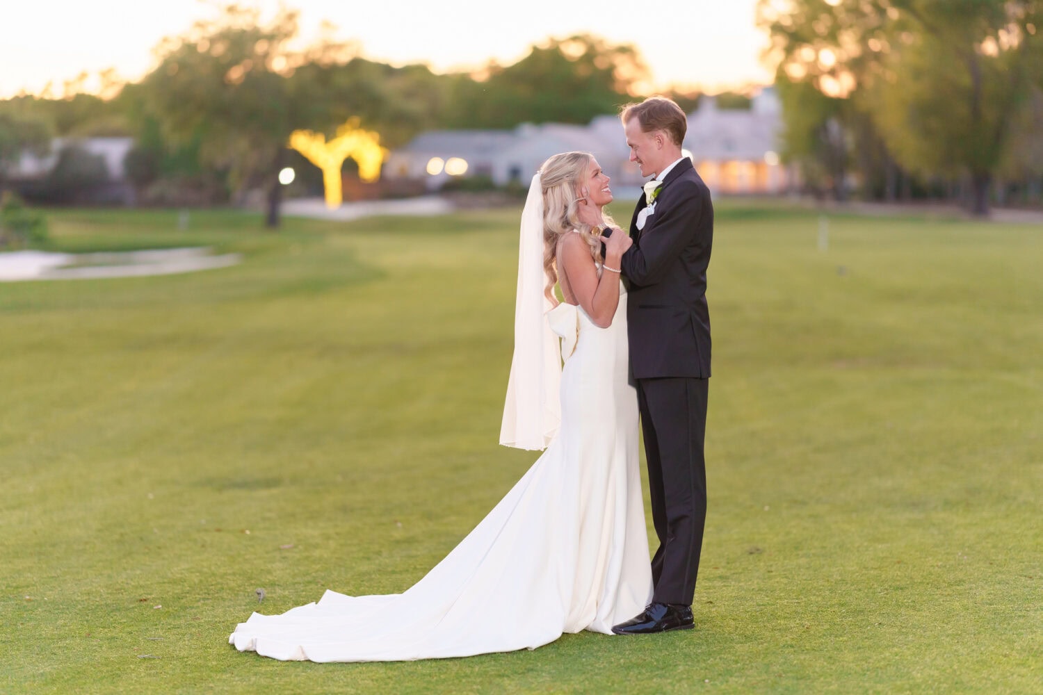 Groom pulling bride in for a kiss with the lights of the clubhouse in the background - Pawleys Plantation